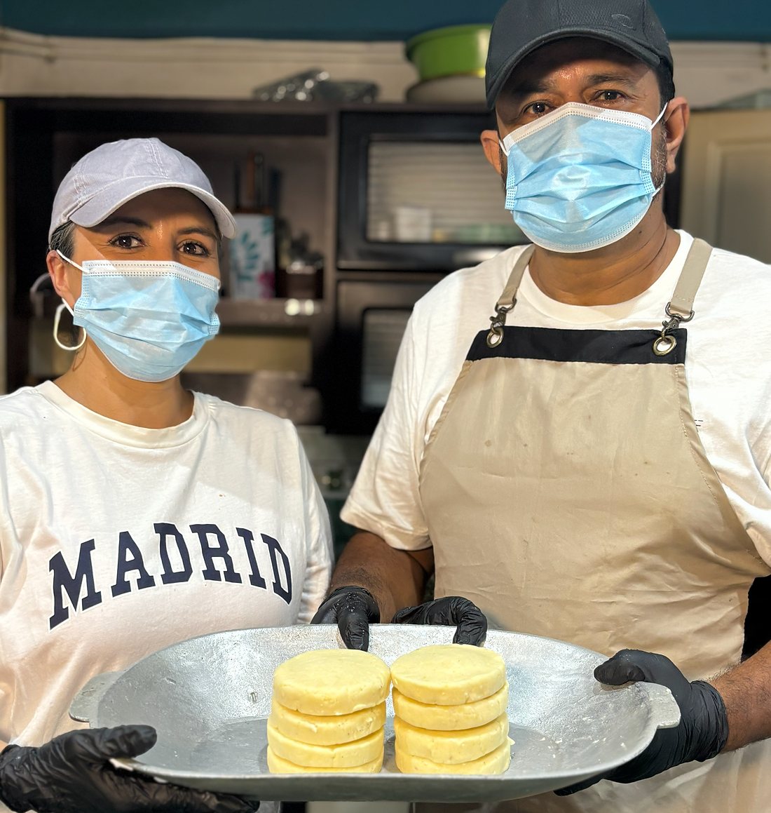 Las manos detrás de Arepas Quesudas con una bandeja de arepas recién hechas